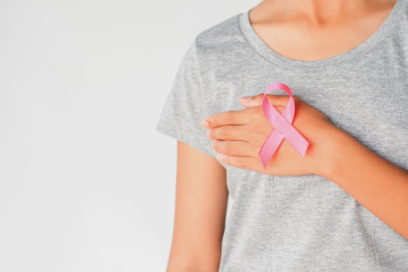 Woman covering her breast and with a breast awareness ribbon on her hand